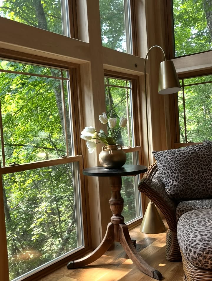 A sunlit window corner with natural wood trim, antique table and flowers, styled by Kristin Saunders